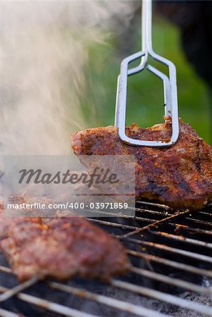 Grilled chuck steak hold in metal tongs. Shallow depth of field.