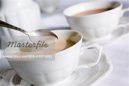 Tea or coffee set - teaspoon over two porcelain cup on the table, one with milk. Shallow depth of field (focus on teaspoon).