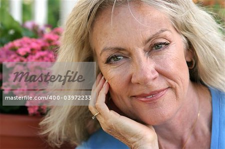 A beautiful mature blond woman relaxing in her garden, wearing a confident expression.