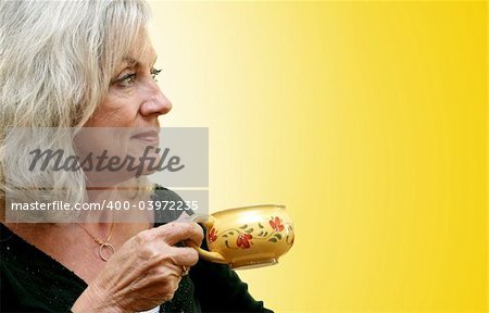 A beautiful mature woman enjoying a cup of coffee as the sun comes up.  Golden background with gradient applied.