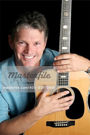 A handsome musician posing with his guitar.  Black background.