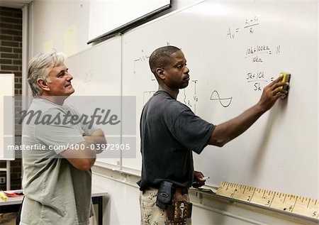 A teacher looks on as his adult education student erases the board.