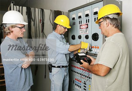 Electricians working on an industrial power distribution center while supervisor watches.  All work being performed according with industry code and safety standards.