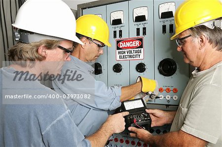 Group of electricians using an OHM meter to test voltage in an industrial power center.  All work being performed according to industry code and safety standards.  (note to inspector: OHMS on the meter is a unit of measurement not a trademark)