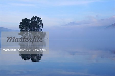 Small tree-covered island rises out of the mist on Loch Tay, Perthshire, Scotland