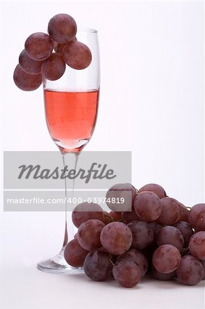 A glass of rose wine with grapes against a plain background.