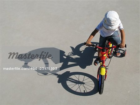 A little boy riding a bike with his shadow on a gray background