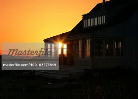 A glimpse of the sun that is shining through a window in a vacation house. The golden colors of sunset together with the halo and rays of light from the sun provide a tranquil scene.