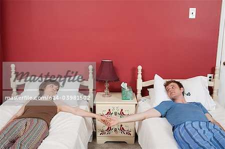 Young couple lying on single beds, holding hands