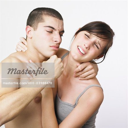 A young couple on a white background. They are holding each other and look as if they are having a fight. The man is holding his fist up threateningly, but the woman has a hint of a smile on her face. Maybe they are just playing. Both models have their eyes closed.