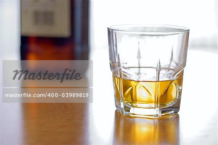 Glass of yellow whiskey and brown bottle on the table