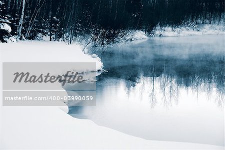 A winter landscape showing a foggy river in blue tones