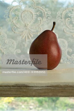 Red Pear on a white wooden shelf in front of a window with muslin  curtain