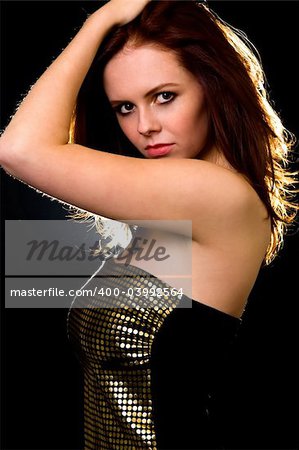 Attractive young brown hair woman standing sideways with hand over head with serious expression backlit over black