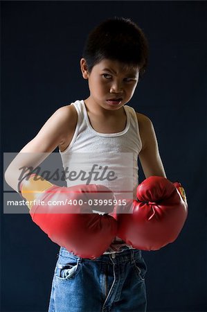 Young asian boy with mean expression wearing red boxing gloves standing on black background