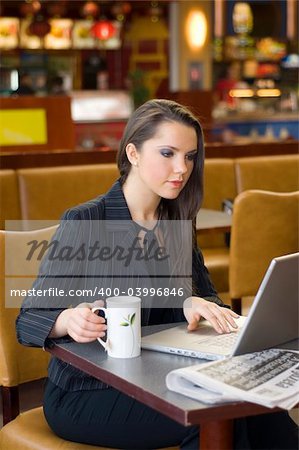 pretty woman sitting in a cafe with a cup of tea working on laptop