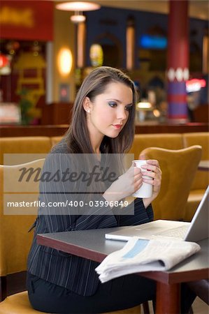 young business woman in a bar watching laptop and drinking tea