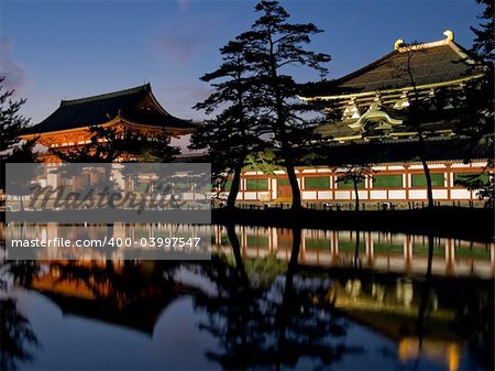 Illuminated evening view of the inner gate and wall surrounding Todai-ji temple (called Todai-ji Chuu-mon) with a pond in the foreground in Nara, Japan.  Todai-ji temple can be seen in the background behind the wall. Todai-ji, reputedly the largest wooden building in the world, houses a colossal bronze statue of the Buddha Vairocana, known in Japanese as the Daibutsu.