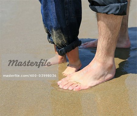 Man's and child's feet in the sand at a beach