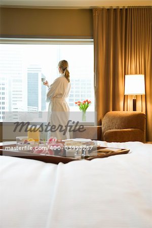 Bed in breakfast tray laying on bed with mid-adult woman in background.