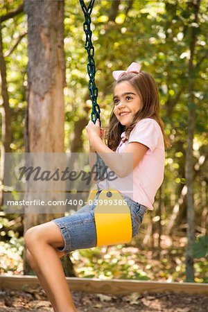 Hispanic girl swinging and smiling.