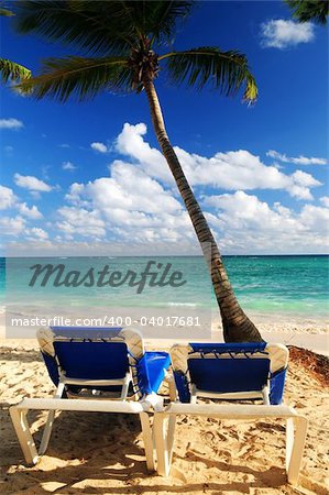 Sandy beach of tropical resort with palm trees and two reclining chairs