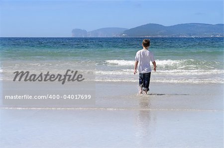 Sardinia, little boy playing on a white sandy Alghero beach,  Capo Caccia in the background