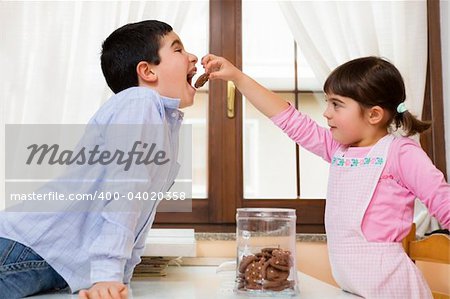 little girl giving a cookie to her brother in the kitchen