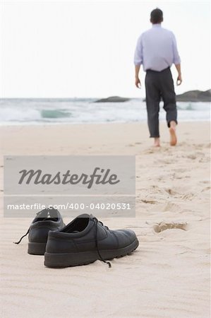 Businessman walking barefoot on a beach. Focus on his shoes in the foreground.