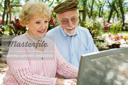 Happy senior couple on their laptop computer in a beautiful outdoor setting.