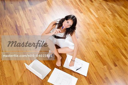 Young woman sitting in new home with laptop an blueprints, high ancle view