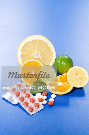 Citrus slices, halves and full fruits with pills on a blue surface
