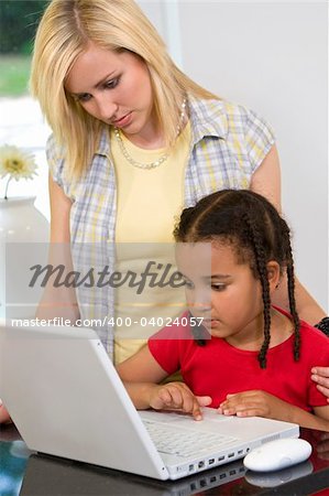 A beautiful young mother and her mixed race young daughter using a laptop at home in the kitchen.