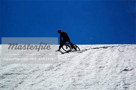 Sky, snow and mountain biker - downhill from mountain pass