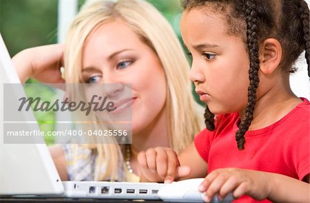 A beautiful young mother and her mixed race young daughter using a laptop at home in the kitchen.