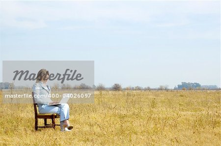 A young business woman working on a laptop in the middle of a dry field.