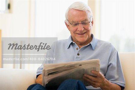 Man in living room reading newspaper smiling