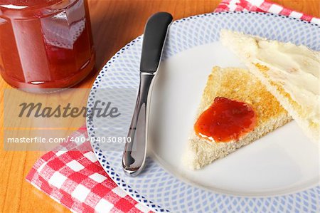 Toast with butter and strawberry jam glass jar in the white plate with soft shadow on square mat background. Shallow depth of field