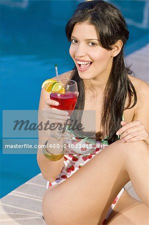 A beautiful young Hispanic woman drinking a cocktail with a swimming pool in the background