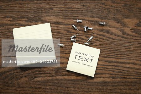Yellow sticky note pads with silver push pins on oak wood