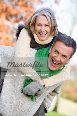 Senior man giving woman piggyback ride through autumn woods