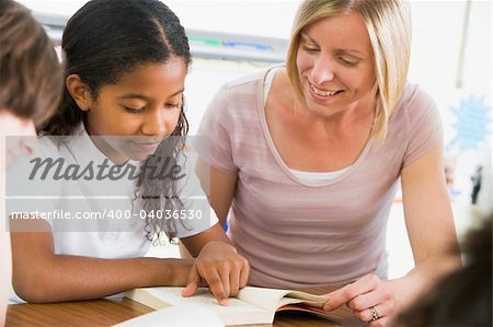 A schoolgirl and her teacher reading a book in class