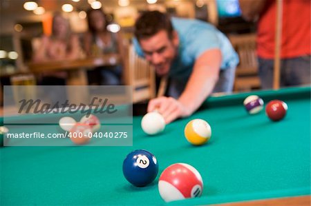 Young man playing pool in a bar (focus on pool table)