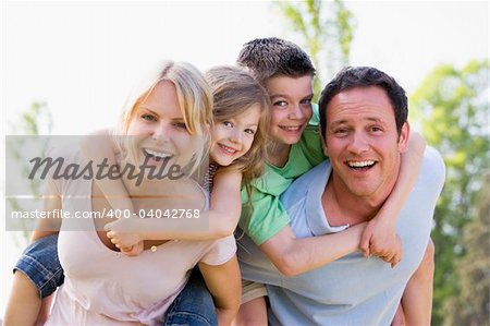 Couple giving two young children piggyback rides smiling