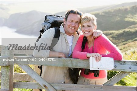 Couple on cliffside outdoors leaning on railing and smiling