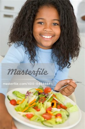 Girl sitting at table eating salad at home