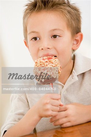 Young boy indoors eating candy apple