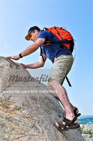 Middle aged man with backpack climbing a rock