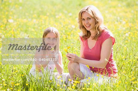 Mother and daughter outdoors holding flower smiling