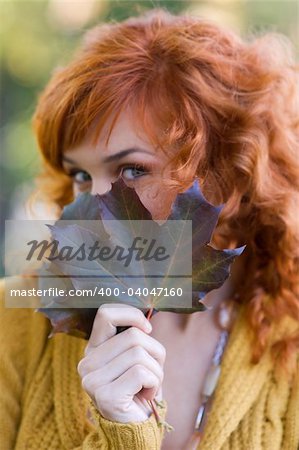 close up of red-haired woman behind a leaf in park focus on leaf